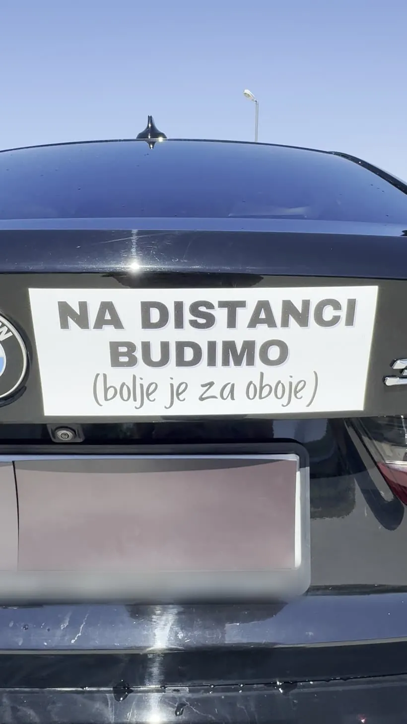 Magnetna tabla „Na distanci budimo” na gepeku crnog automobila