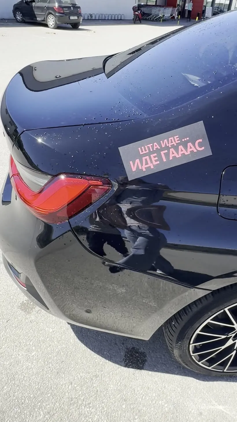 Magnetna tabla sa ćiriličnim natpisom „Šta ide… ide gaaas” na zadnjem blatobranu mokrog crnog auta