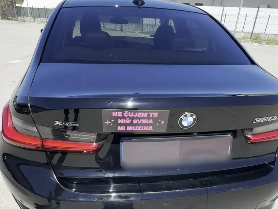 Magnetna tabla „Ne čujem te, niš’ svira mi muzika” sa roze slovima na gepeku crnog BMW-a