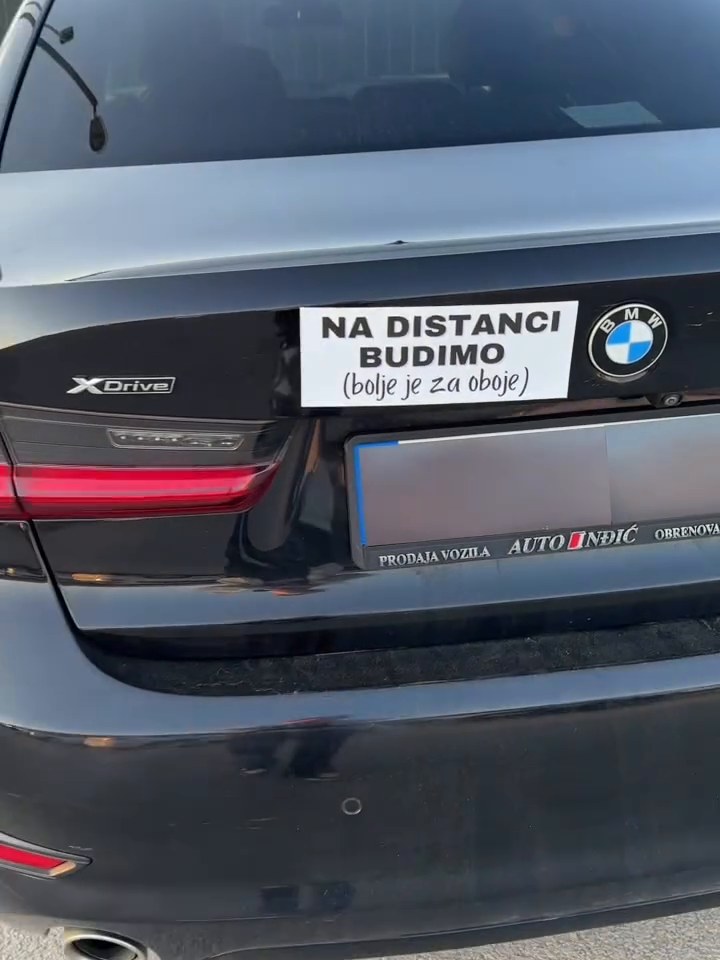 Bela tabla „Na distanci budimo” na gepeku crnog BMW-a
