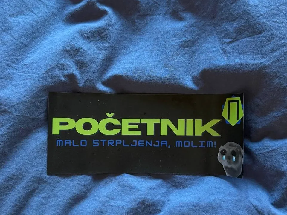 Magnetna tabla „Početnik, malo strpljenja, molim!” sa zelenim slovima, položena na plavu tkaninu