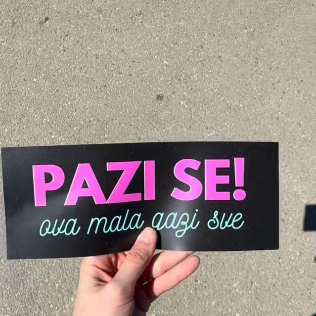 Ruka drži magnetnu tablu „Pazi se! ova mala gazi sve” iznad asfalta
