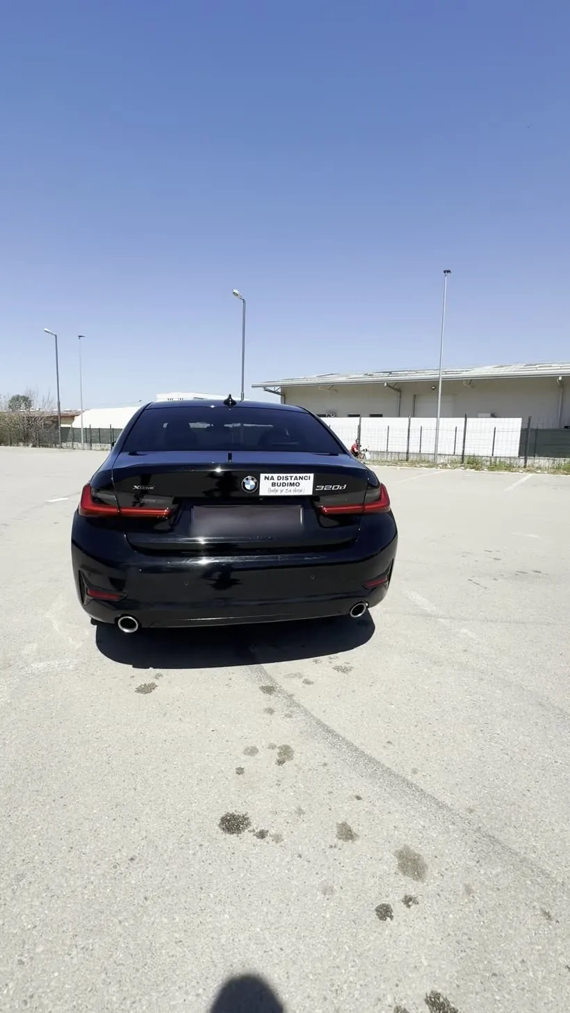Crni BMW otpozadi sa magnetnom tablom „Na distanci budimo” na poklopcu gepeka