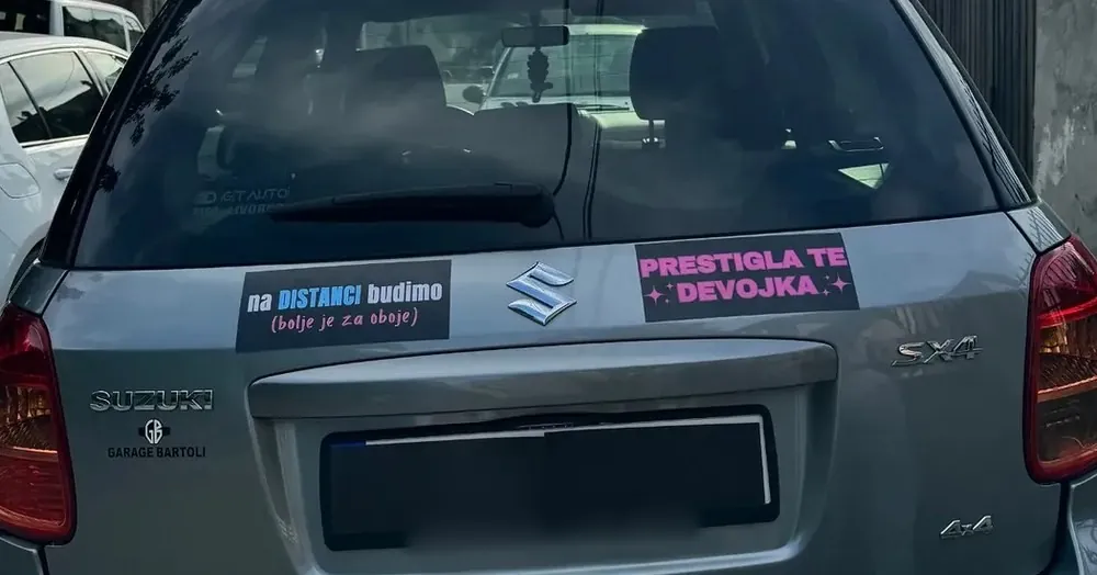 Dve magnetne table na gepeku jednog auta: „Na distanci budimo” i „Prestigla te devojka”